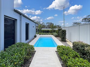 A modern building with a swimming pool, surrounded by well-maintained hedges and a clear sky.