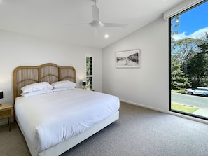 Quarto com cama, ventilador de teto, janela com vista exterior e quadro na parede.