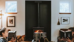 A cozy living room with a fireplace, a sofa, and a person reading a book. - Evergreen Escape •Hot Tub •Sauna •AC •Workspace! (Gold Bar)