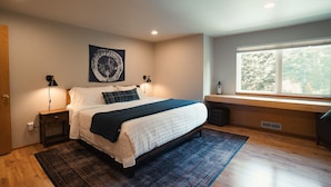 A bedroom with a bed, bedside lamps, a window, and a view of trees. - Evergreen Escape •Hot Tub •Sauna •AC •Workspace! (Gold Bar)