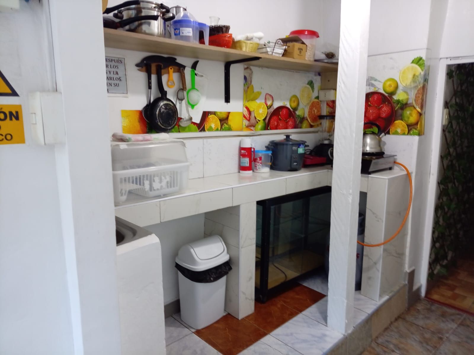 Uma cozinha com pia, lixeira, geladeira e diversos utensílios e eletrodomésticos.
