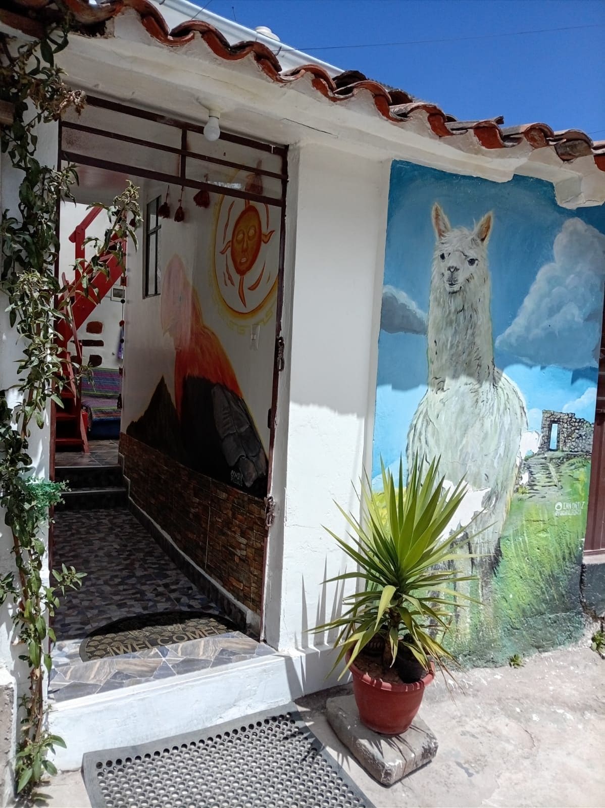 Entrada de un edificio con un mural de una llama, una escalera y un felpudo.