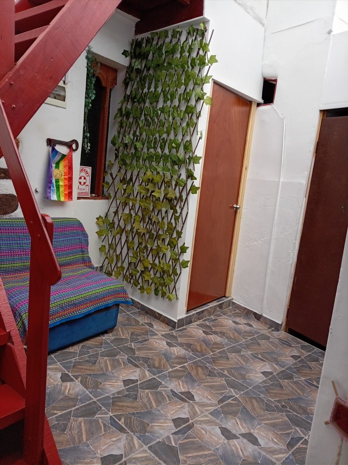 Una habitación con suelo de baldosas, una escalera, una planta en la pared y una puerta.