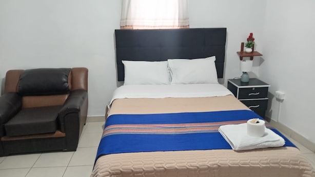 Habitació d'hotel amb un llit, una cadira, una tauleta de nit i una finestra amb cortines.