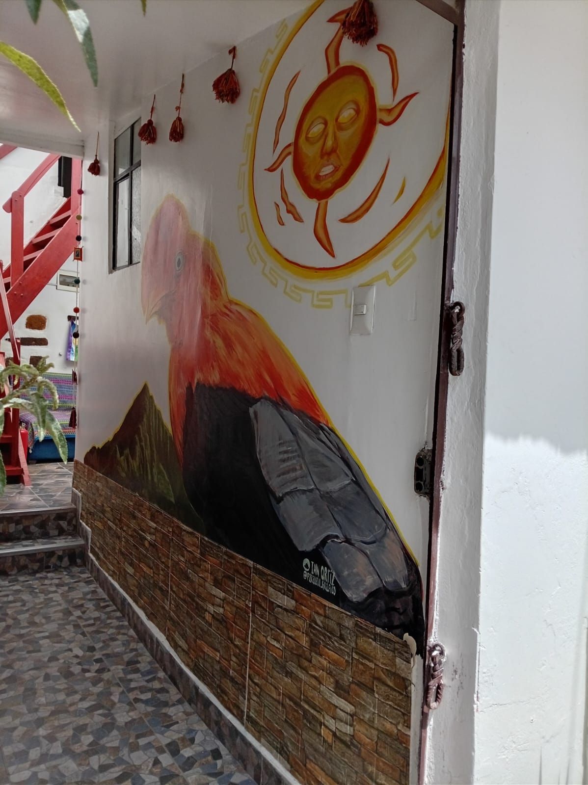 A hallway with a mural of a bird and sun, a staircase, and a tiled floor.