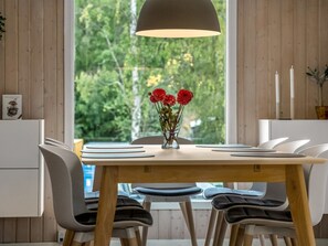 Ein Essbereich mit einem Holztisch, weißen Stühlen, einer Vase mit roten Blumen und einer Pendelleuchte.