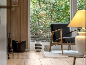 Ein Zimmer mit Holzboden, einem schwarzen Stuhl, einer gestreiften Vase und einem Fenster mit Blick auf Grünflächen.