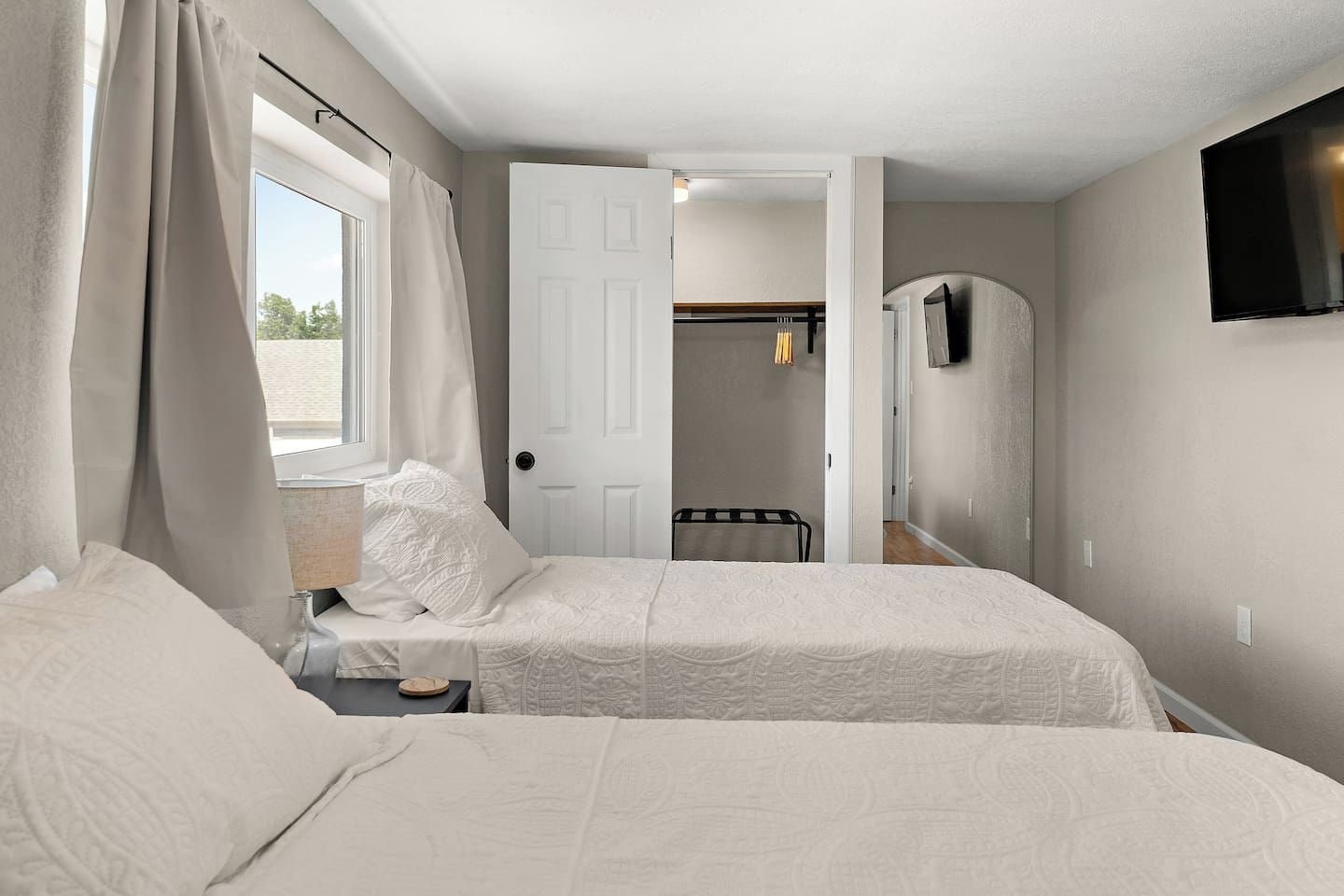 Un dormitorio con dos camas, un televisor montado en la pared y una puerta que da a otra habitación.