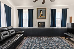 A living room with a black leather sofa, a patterned rug, a fireplace, and a television. - The Blue Perch - A Local Hidden Gem (Pueblo)