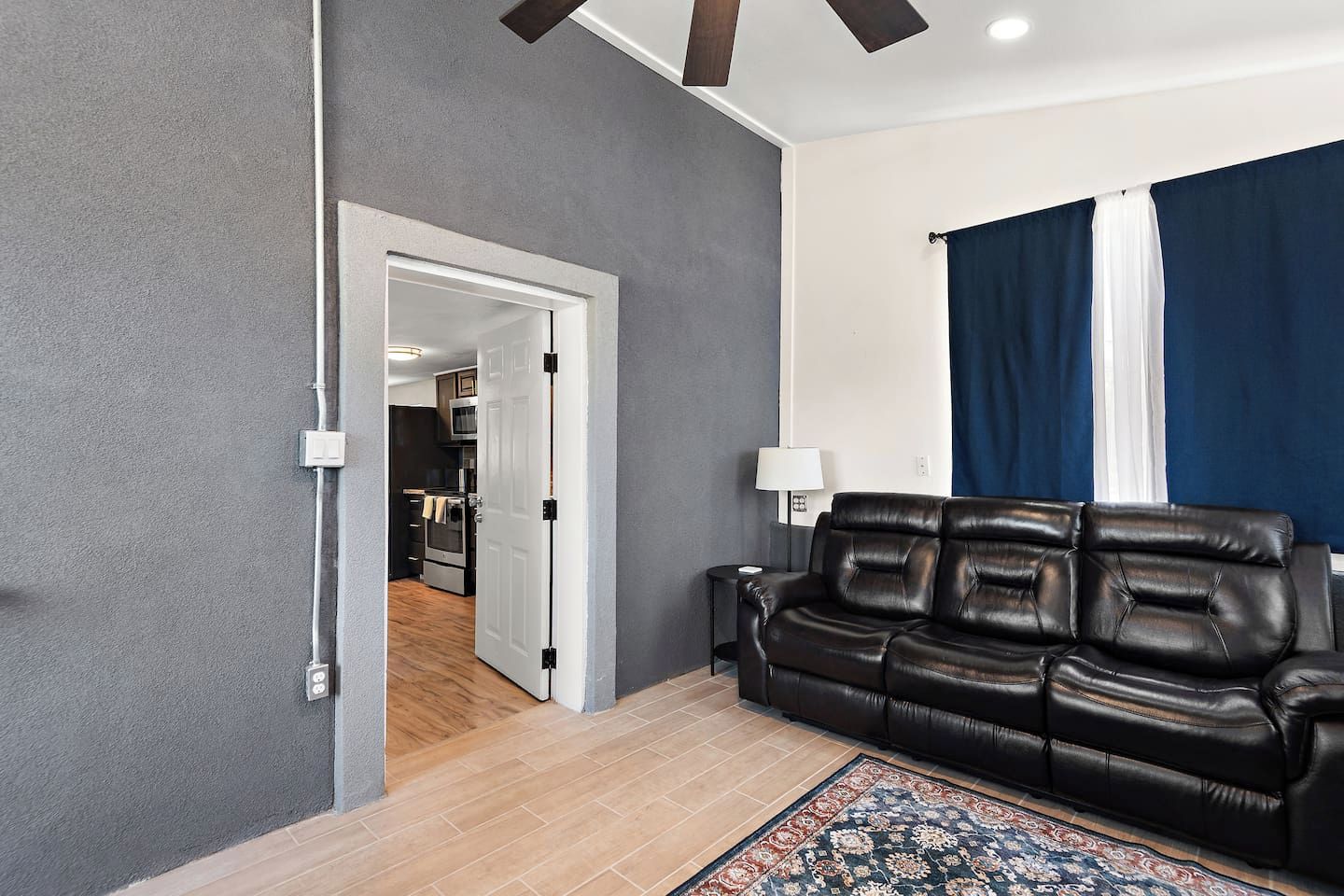 Una sala moderna con un sofá de cuero, un tapete estampado y vista a una cocina a través de una puerta abierta.