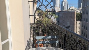Un balcon avec une table et des chaises en métal, des plantes en pot et une vue sur les bâtiments de la ville.