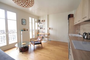 Una cocina moderna con armarios de madera, una zona de comedor con sillas, una estantería y un ventanal que proporciona luz natural.