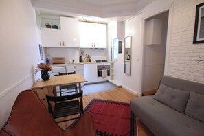Ein kompakter Wohnraum mit einer Küchenzeile, einem Essbereich mit Tisch und Stühlen sowie einem grauen Sofa.