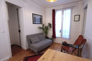 Une pièce avec un canapé gris, une table en bois, un rideau rouge et un tableau encadré au mur.