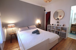 Ein Schlafzimmer mit einem Bett, Nachttischlampen, einem Spiegel, einem Bücherregal und einem Holzboden.