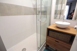 Ein modernes Badezimmer mit einer Duschkabine aus Glas, einem Holzlagerfläschchen mit einem weißen Waschbecken und einem Spiegel darüber.