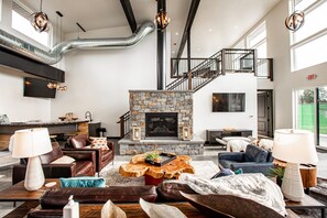 A spacious living area with a stone fireplace, leather sofas, and a modern staircase. - Top-floor corner condo l Hot Tub / Summer Pool / Gym (Whitefish)