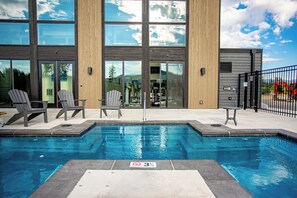 Une piscine avec un panneau indiquant qu’il est interdit de plonger, entourée de chaises longues et bordée d’un bâtiment aux grandes fenêtres.