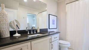 Ein Badezimmer mit einer weißen Toilette, einer schwarzen Ablage, einem großen Spiegel und einem gerahmten Bild an der Wand.