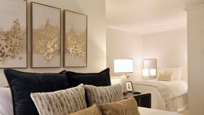 Ein Hotelzimmer mit einem Bett, einem Nachttisch, einer Lampe und drei gerahmten Kunstwerken an der Wand.