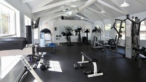 Ein Fitnessraum mit verschiedenen Trainingsgeräten, einer Bank und einem Wasserspender.