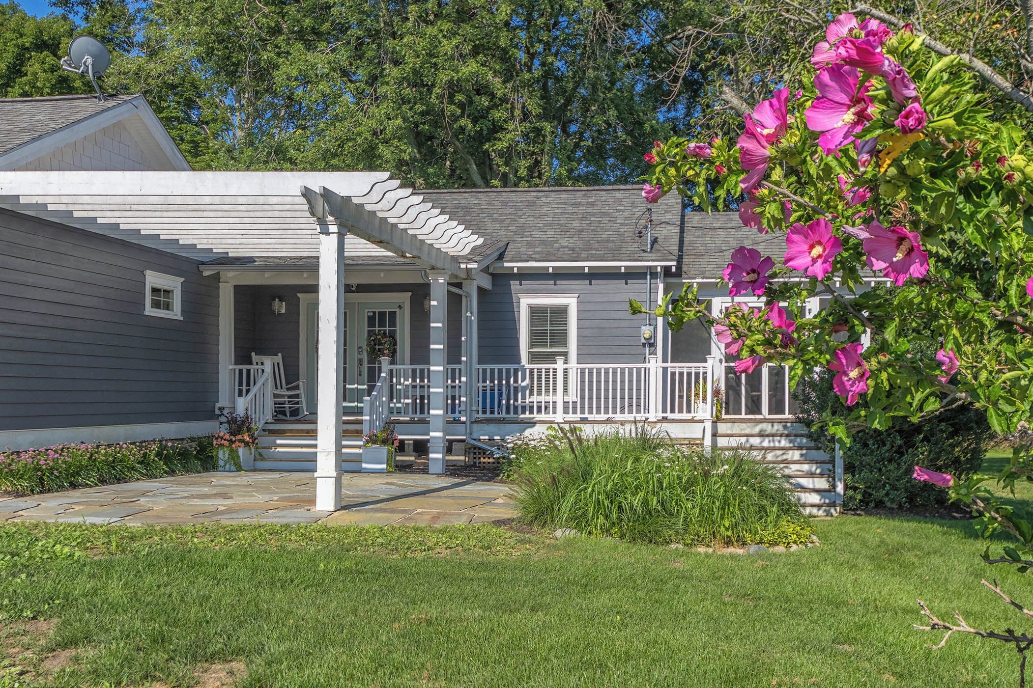 A residential house with a covered porch, a front door, and a small front yard with a lawn and a flowering plant.