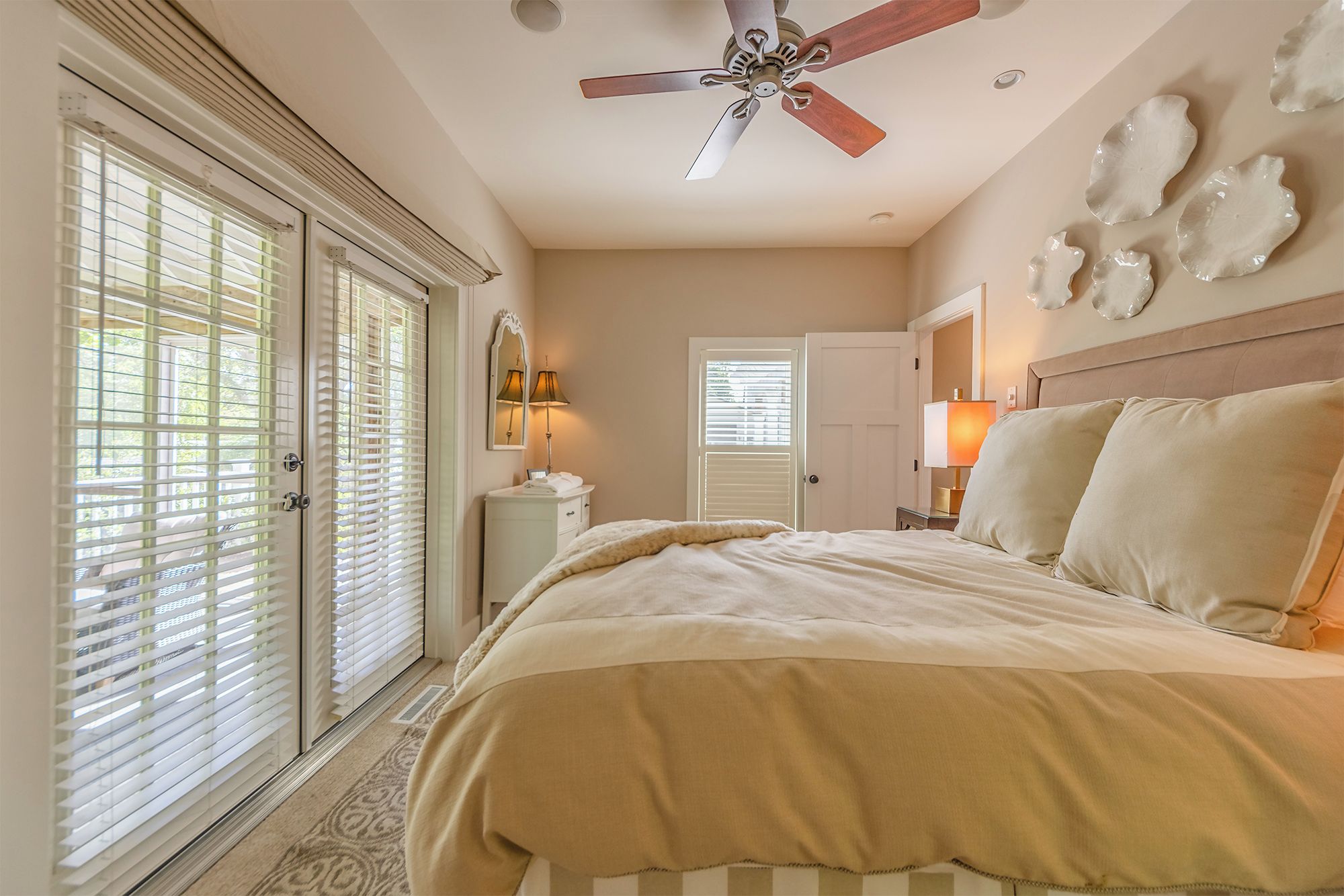 A bedroom with a bed, a ceiling fan, a nightstand, a lamp, and a door leading to another room.