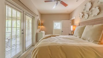 A bedroom with a bed, a ceiling fan, a nightstand, a lamp, and a door leading to another room.
