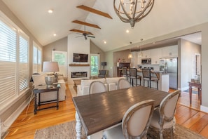 A spacious living area with a dining table, chairs, a fireplace, and a kitchen in the background.