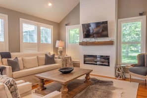 A living room with a sofa, a coffee table, a TV mounted on the wall, and a fireplace.