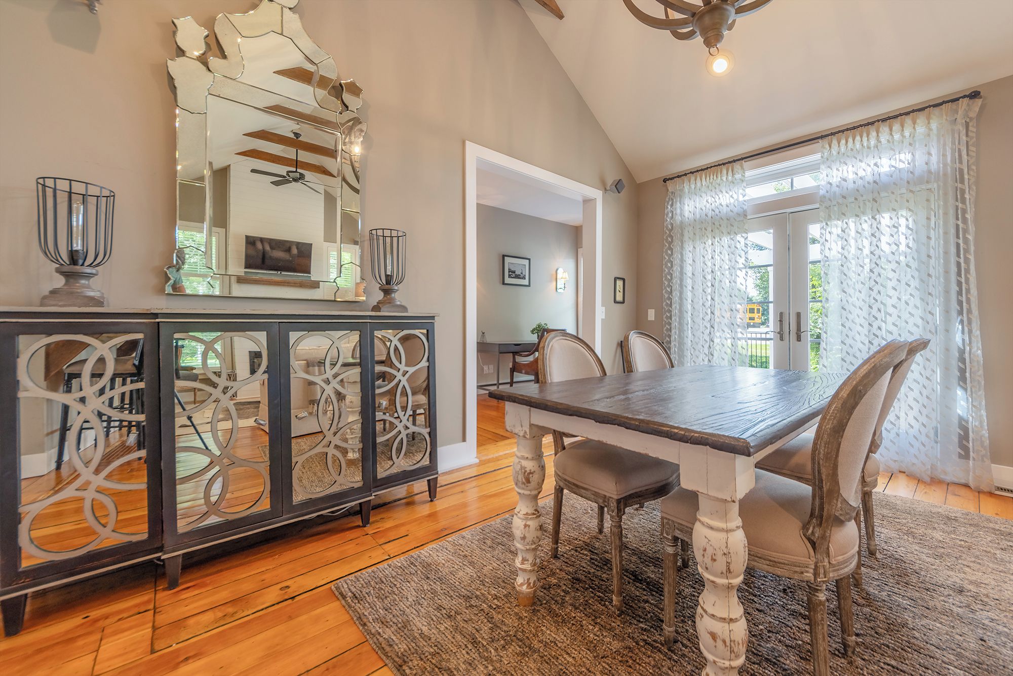 A dining area with a wooden table, chairs, a cabinet with decorative metalwork, and a large mirror on the wall.
