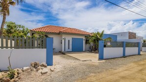 Un edifici residencial amb teulada vermella, façana blanca i blava i entrada tancada per una reixa.