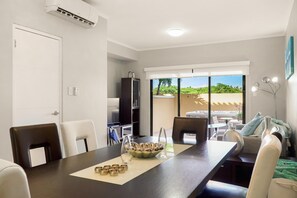 A dining area with a long table, chairs, and a central decorative bowl. There is a sliding glass door leading to an outdoor patio with a view of greenery. - Private HotTub Escape:ModernLuxe Townhome 2BR3BA (Noord)