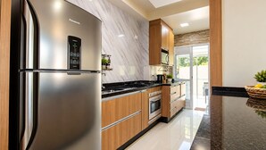 Eine moderne Küche mit einem Edelstahlkühlschrank, Holzschränken, einer schwarzen Arbeitsplatte und Blick ins Freie.