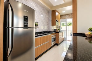Cozinha moderna com geladeira de aço inoxidável, armários de madeira, bancada preta e vista para o exterior.