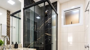 Ein modernes Badezimmer mit einer gläsernen Dusche, einer weißen Toilette und einem Waschbecken mit Granitplatte.