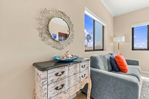 A living room with a decorative mirror, a vintage dresser, a grey sofa with colorful cushions, and a view of palm trees through the windows. - Private Pool Paradise: Luxe Resort Living (Noord)