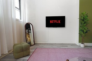 A room with a flat-screen TV mounted on the wall displaying 'NETFLIX,' a mirror, a green bean bag chair, and a potted plant.