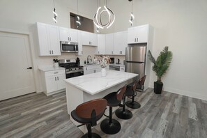 A modern kitchen with white cabinets, stainless steel appliances, a marble countertop, and a central island with bar stools.