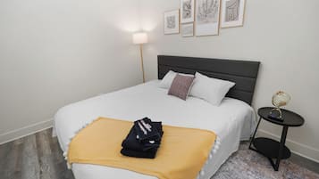 A neatly made bed with a white comforter and a yellow throw blanket, a bedside table with a globe and remote control, and a wall with framed artwork.