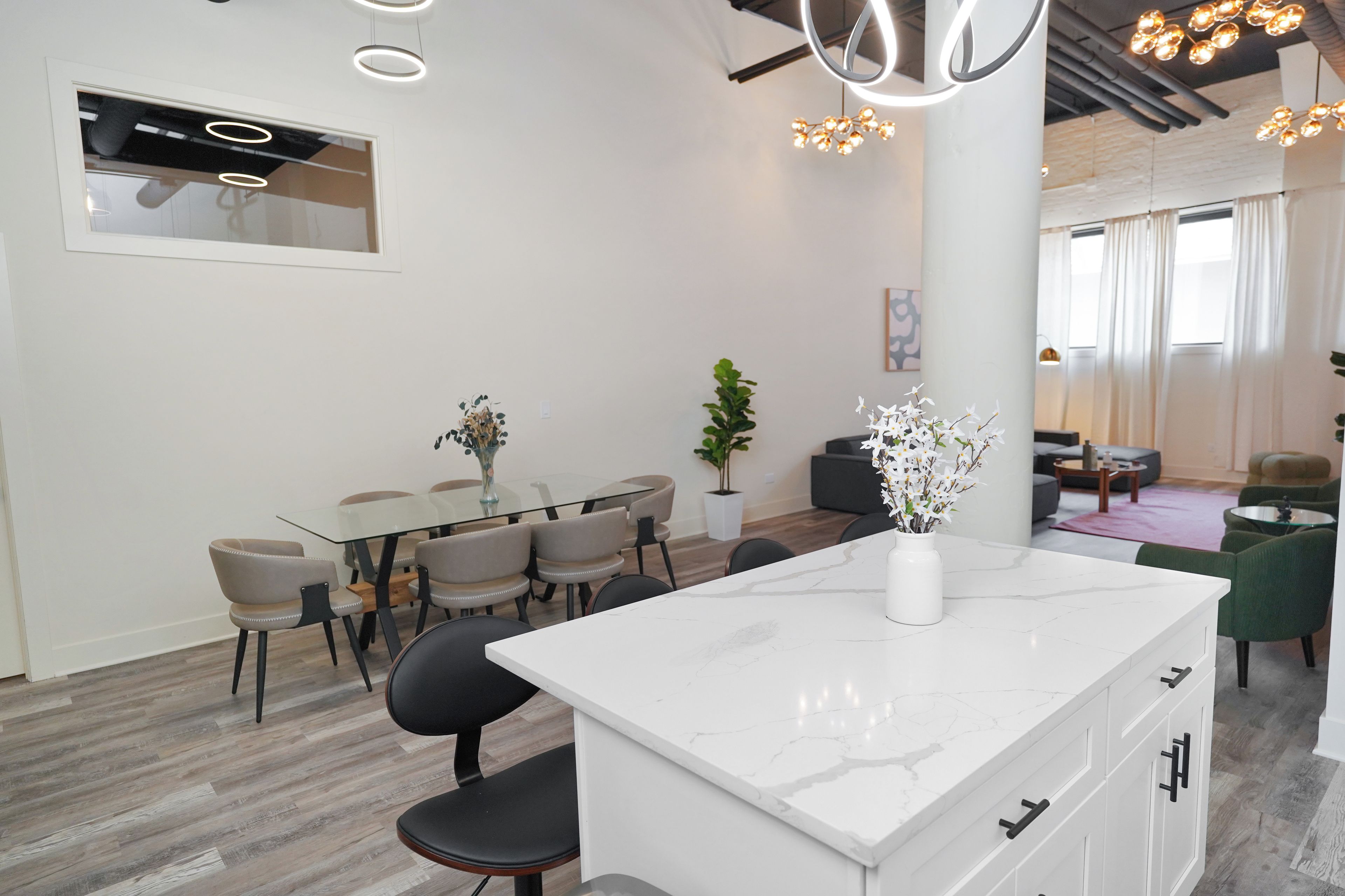 A modern kitchen with a marble countertop, a dining area with a glass table and chairs, and a living area with a sofa and a coffee table.
