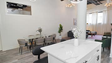 A modern kitchen with a marble countertop, a dining area with a glass table and chairs, and a living area with a sofa and a coffee table.