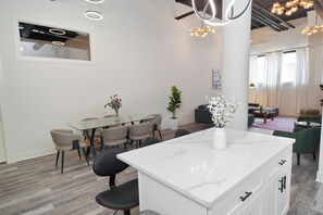 Eine moderne Küche mit Marmorarbeitsplatte, ein Essbereich mit Glastisch und Stühlen sowie eine Wohnarea mit Sofa und Couchtisch.