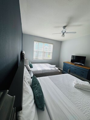 Ein Hotelzimmer mit zwei Betten, einem Deckenventilator, einem Fernseher und einem Fenster mit Jalousien.