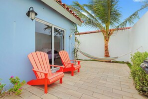 Eine Terrasse mit zwei roten Adirondack-Stühlen, einer Hängematte und einer Palme.