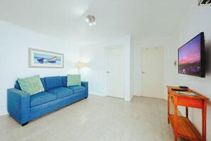 A living room with a blue sofa, a painting, a television, and a wooden table. - Charming & Private - 1BR/1BA - 3 min Palm Beach (Noord)