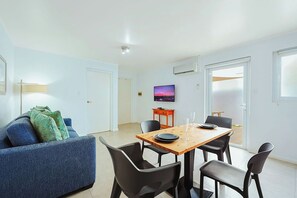 Ein modernes Wohnzimmer mit einer Couch, einem Esstisch mit Stühlen, einem an der Wand befestigten Fernseher und einer Tür zu einem Außenbereich.