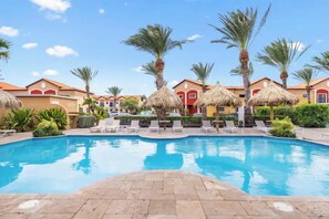A swimming pool with lounge chairs and palm trees, surrounded by buildings with red and yellow facades.
