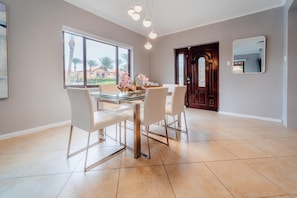 A dining area with a glass table, white chairs, and a view of palm trees through large windows. - Villa Diamante: Luxe Oasis, Gold Coast 4BR 3BA (Noord)