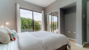 Un dormitori amb un llit gran, un balcó i vistes a vegetació i edificis.